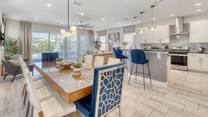 Una cocina moderna con armarios blancos, una isla central y un comedor con mesa y sillas de madera.