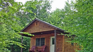 Una cabaña de madera con un porche, dos sillas Adirondack y una puerta.