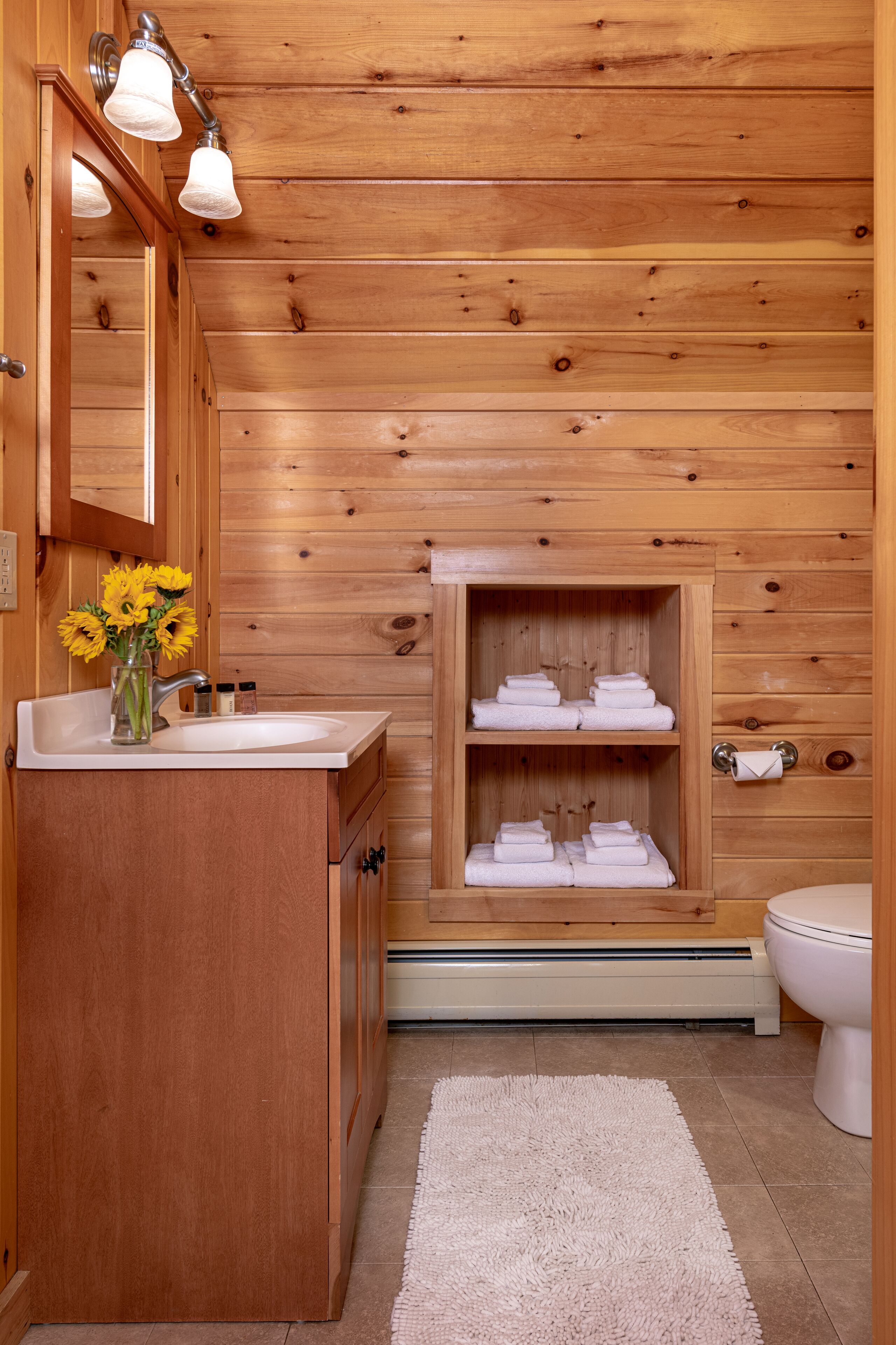 A wooden cabin-style bathroom with a sink, mirror, towel rack, and toilet.