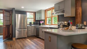 A modern kitchen with stainless steel appliances, wooden flooring, and large windows.