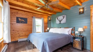 Une chambre aux murs lambrés, avec un lit, un ventilateur de plafond et un luminaire fixé au mur.