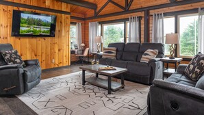 Un salon chaleureux avec un plafond en bois, un téléviseur à écran plat fixé au mur, un ensemble de canapés, une table basse et un tapis.