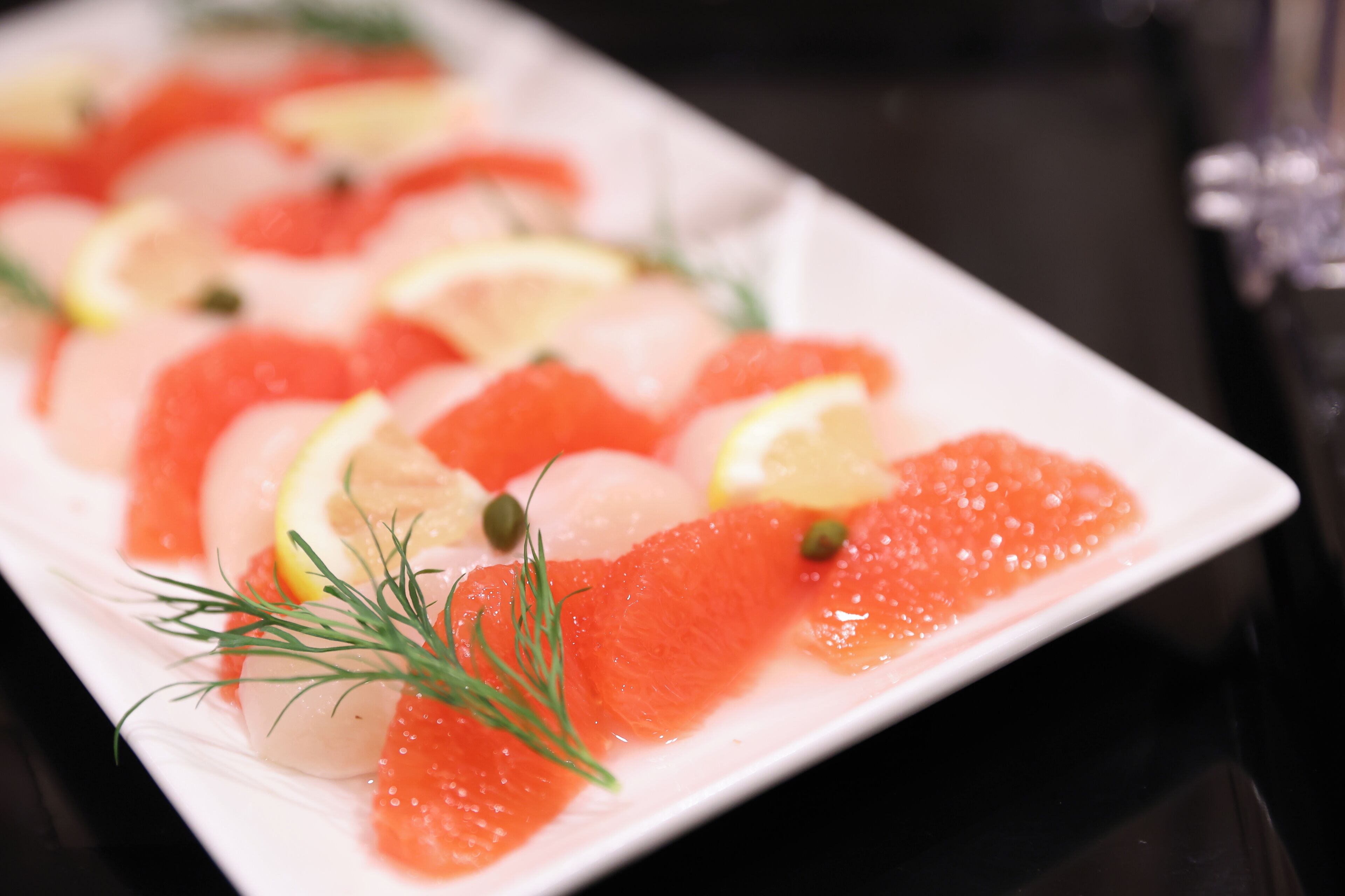 A white rectangular plate with slices of salmon, lemon wedges, and dill garnish.