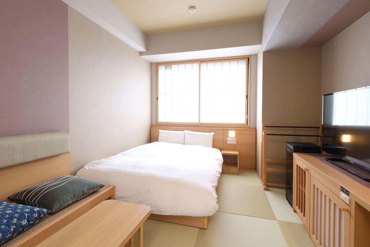 A hotel room with a bed, bedside table, TV, and a window.