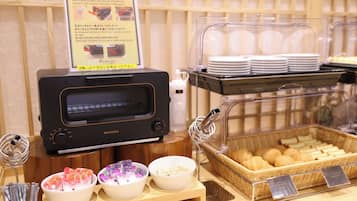 A breakfast buffet with a toaster, bowls of food, and a basket of bread.