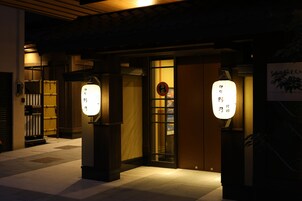 A traditional Japanese building entrance with illuminated signs and a wooden door.