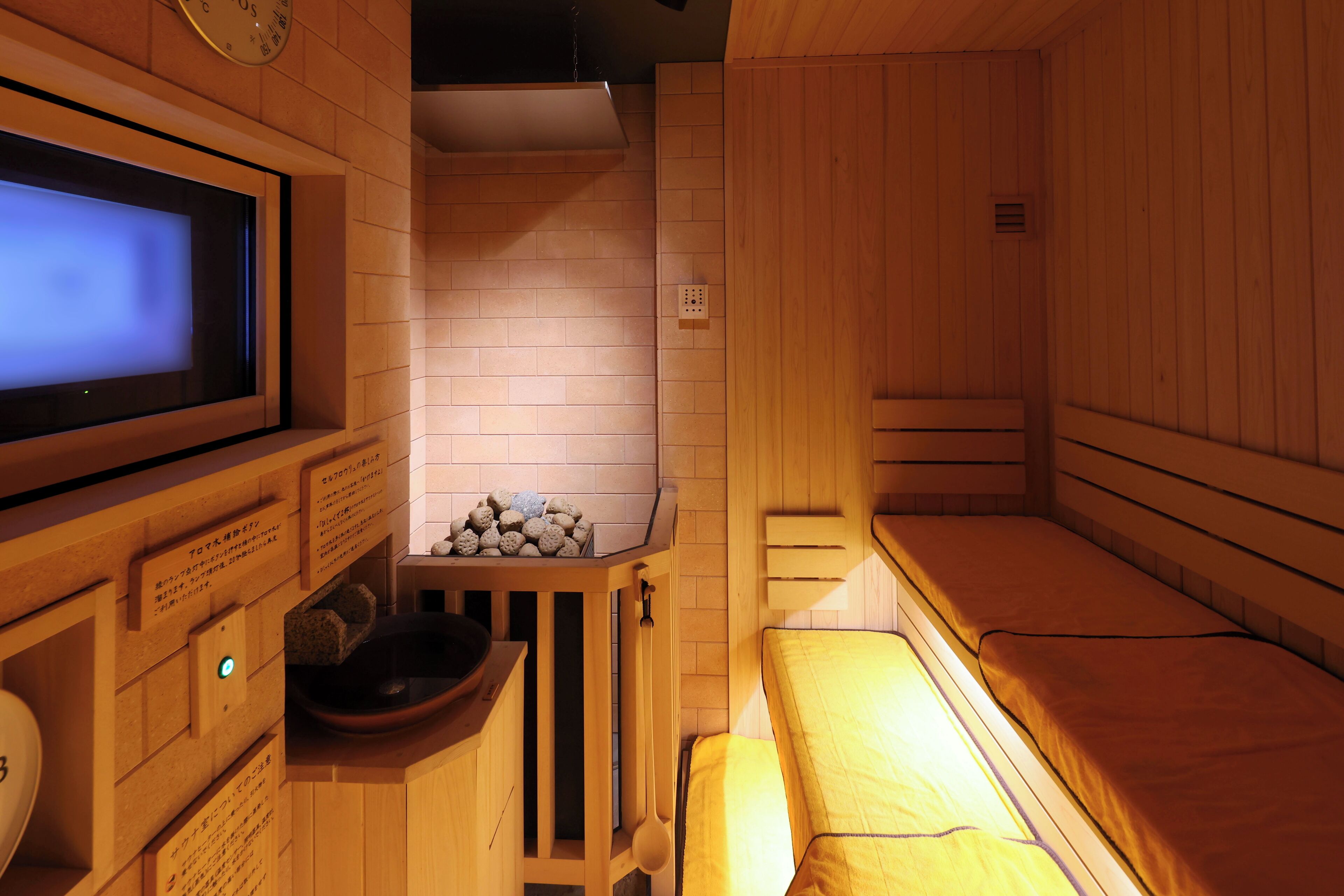 A sauna room with wooden walls, a bench, a television, and a stone basin.