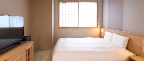 A hotel room with a bed, a TV, a window, and a wooden nightstand.
