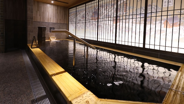 Un onsen japonais traditionnel, avec un banc en bois et une vue sur un paysage montagneux, visible à travers un paravent en papier washi.