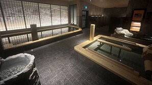 Un espace de bien-être doté d’un bassin en pierre, de bancs en bois et d’un espace clos en verre agrémenté de rochers.
