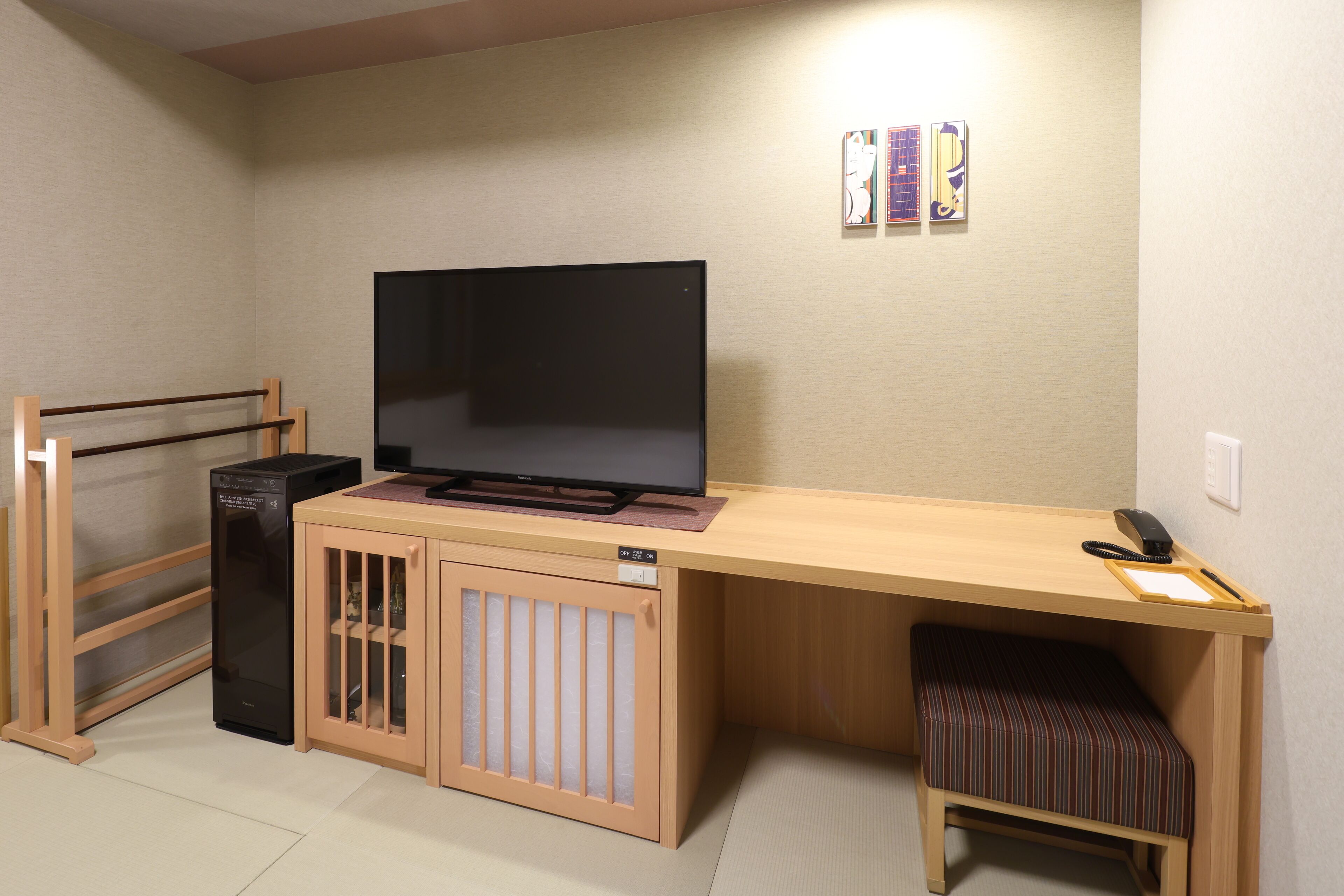 Une pièce de taille modeste, avec un téléviseur posé sur un bureau en bois, un petit banc, une armoire et un radiateur.