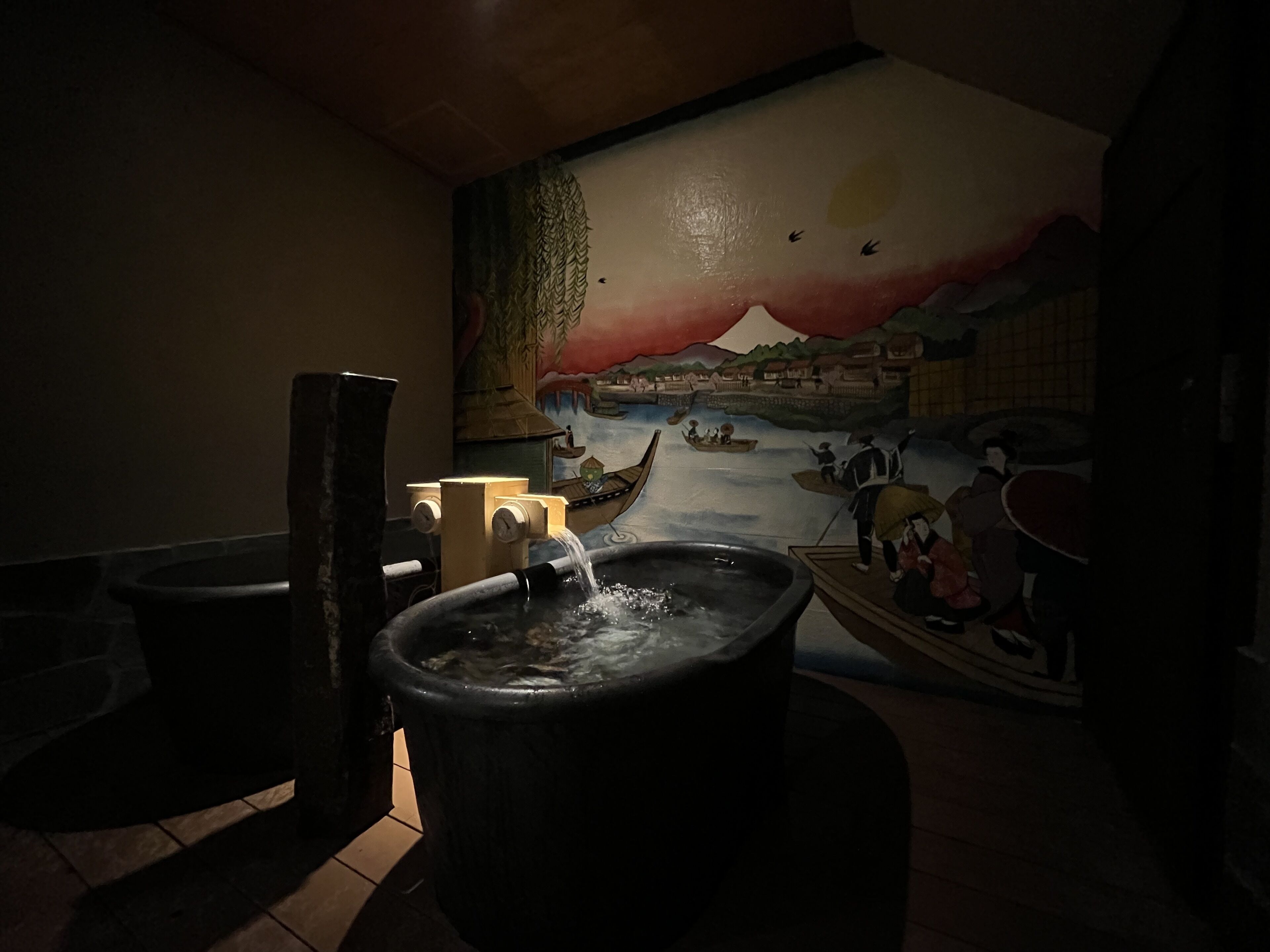 Un bagno con una grande vasca da bagno, un murale raffigurante una scena fluviale e un water.