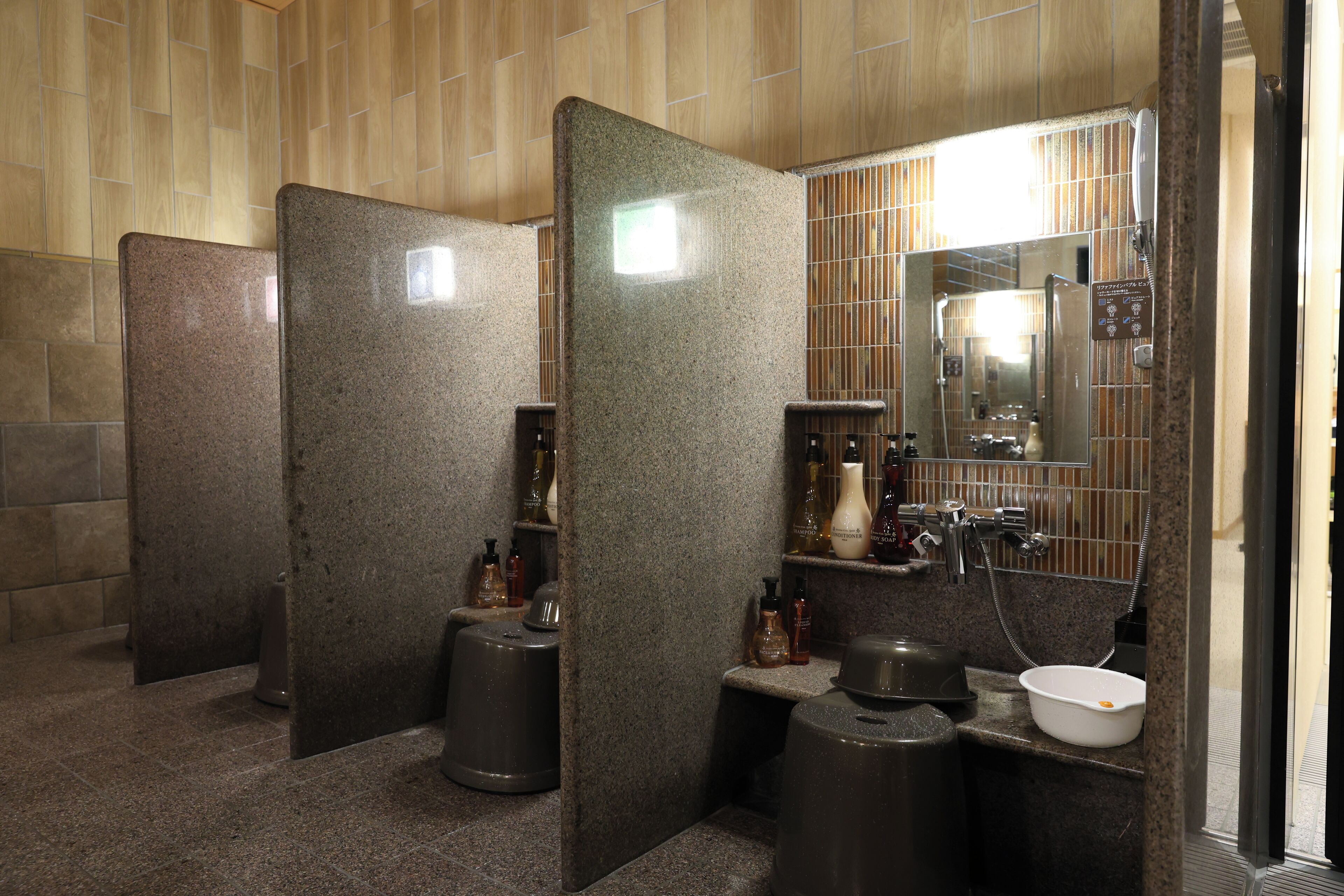 Des toilettes publiques avec des cloisons en granit, un lavabo et un miroir.