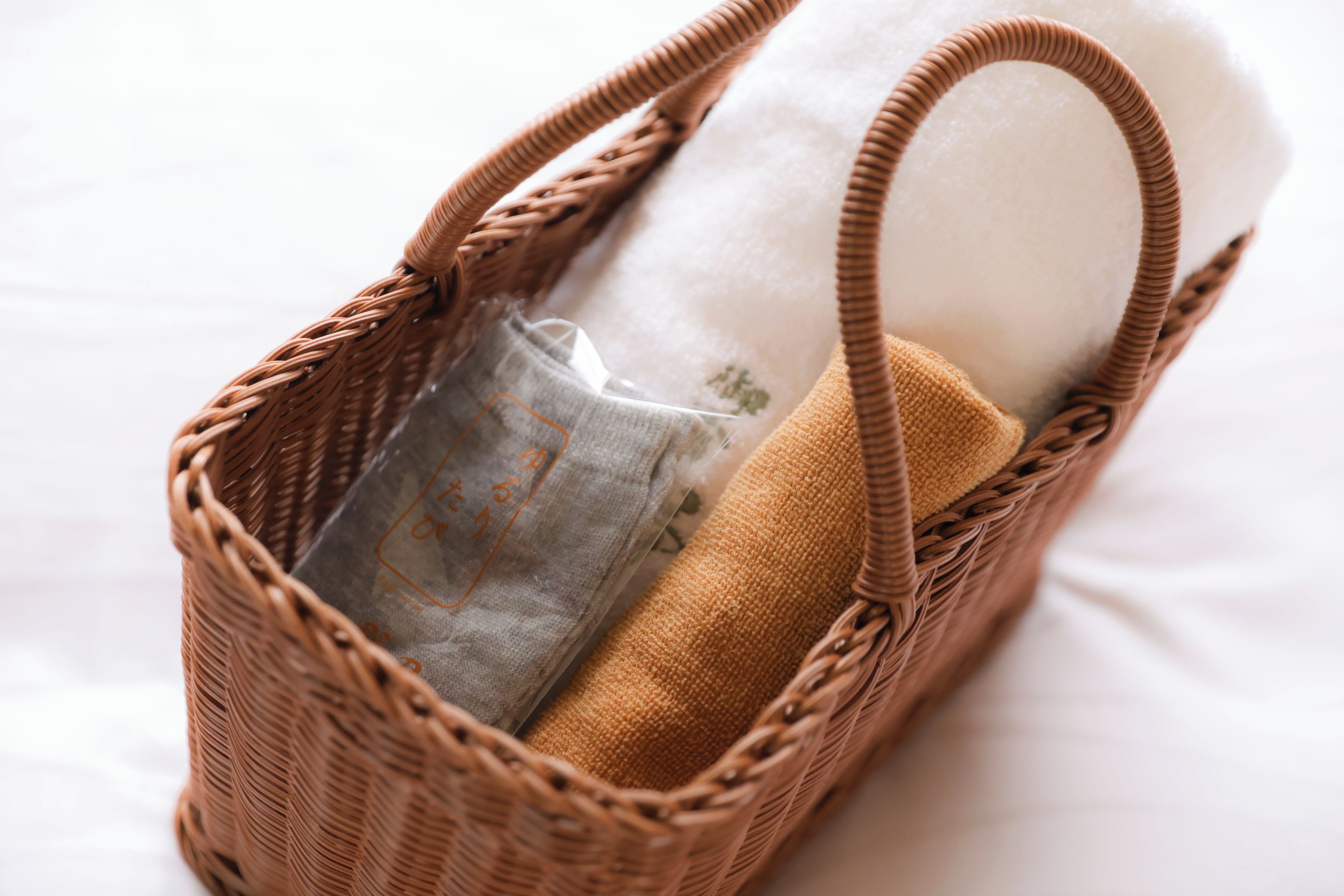 A wicker basket with handles containing rolled-up fabric items.