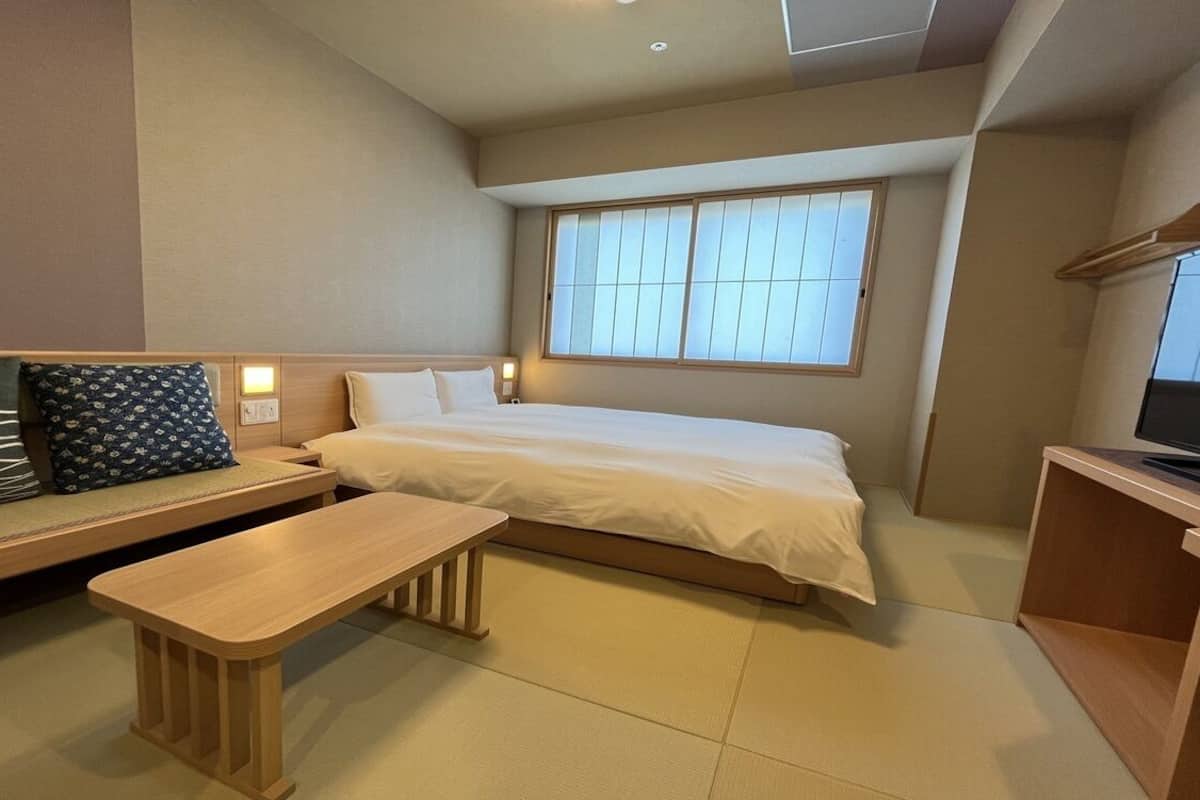 A hotel room with a bed, a bench, a TV, and a window.