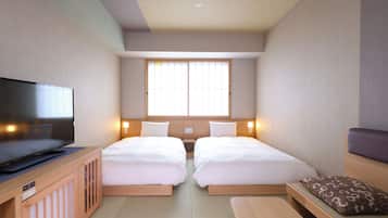 A hotel room with two beds, a television, and a window with blinds.