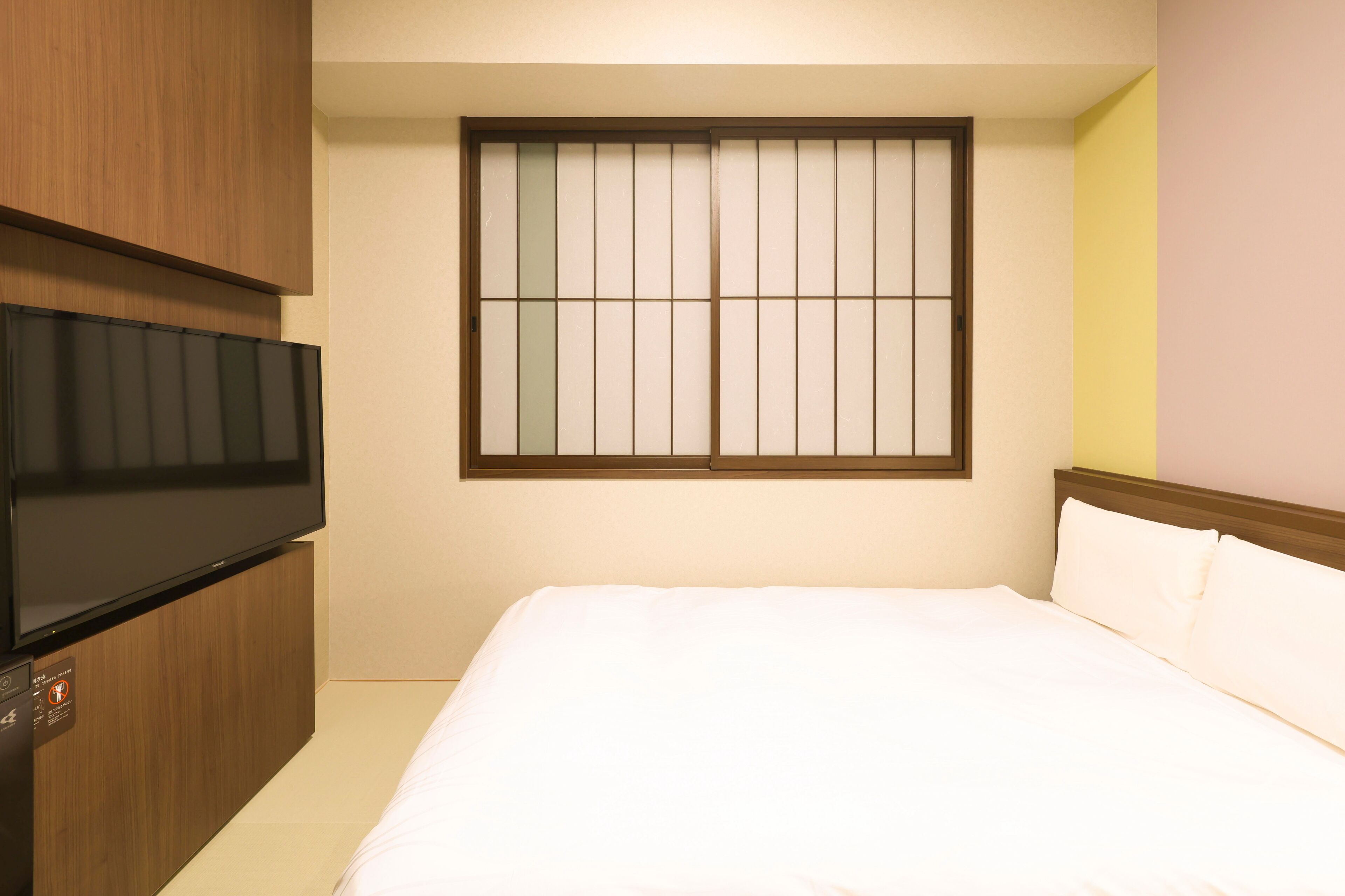 Une chambre d’hôtel avec un lit, un téléviseur posé sur un meuble en bois et une fenêtre à carreaux.