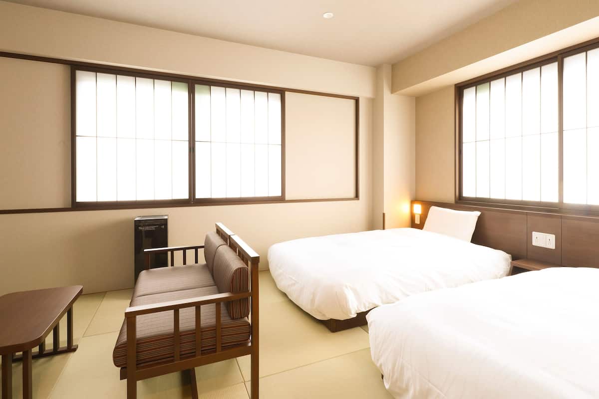 A hotel room with two beds, a wooden desk, and tatami flooring.