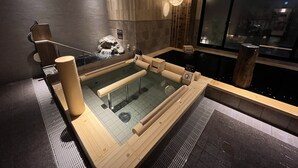 Un spa moderne doté d’un bain à remous, de bancs en bois et d’un mur en pierre.