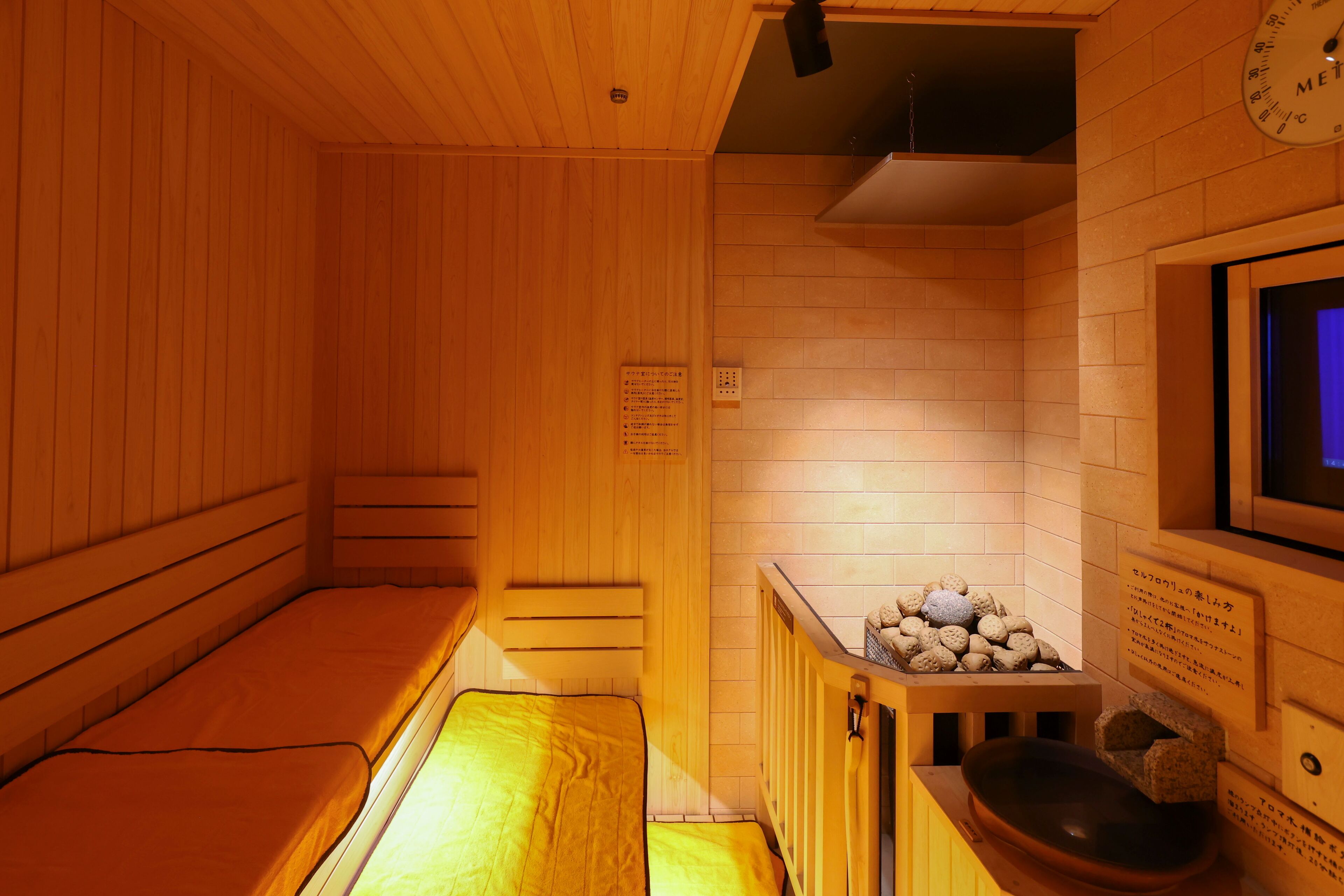 A wooden sauna with benches, a stone basin, and a clock on the wall.