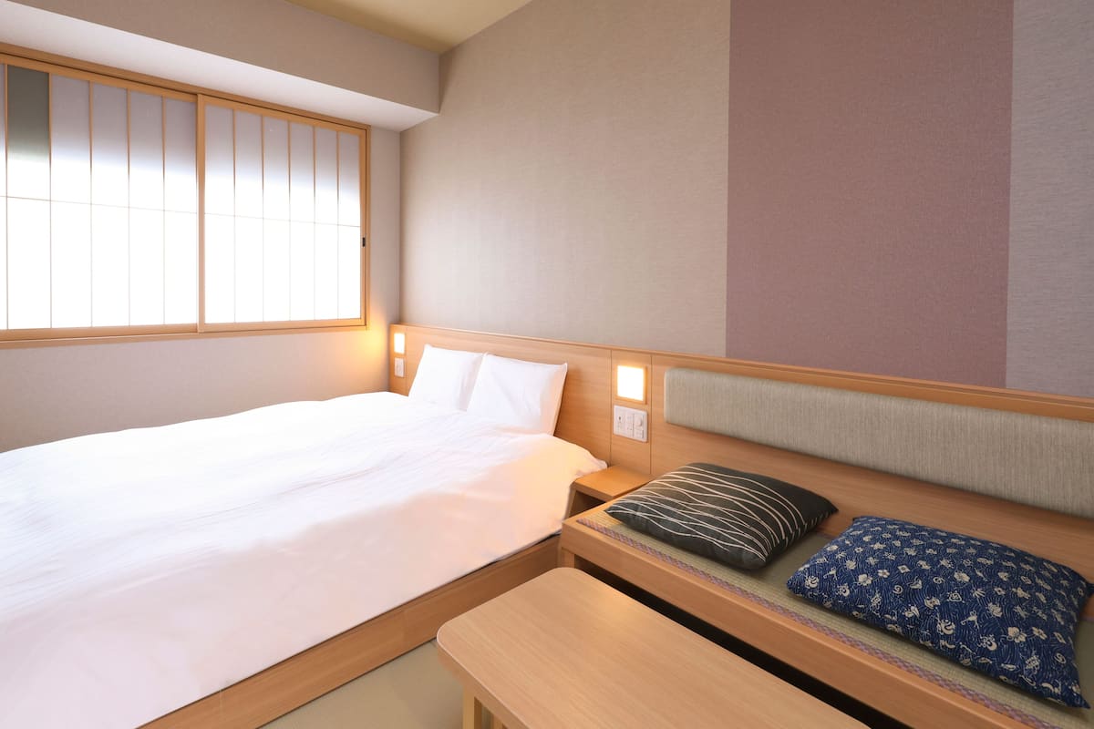 A hotel room with a bed, bedside table, and a seating area with cushions.