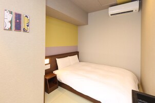 A hotel room with a single bed, a nightstand, an air conditioning unit, and three wall-mounted artworks.