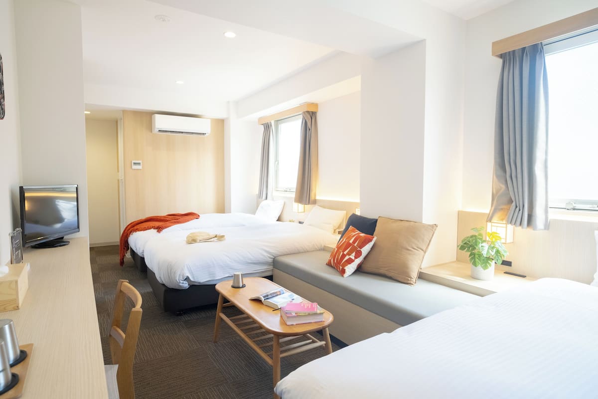 Quarto de hotel com duas camas, uma escrivaninha com cadeira, televisão e janela com cortinas.