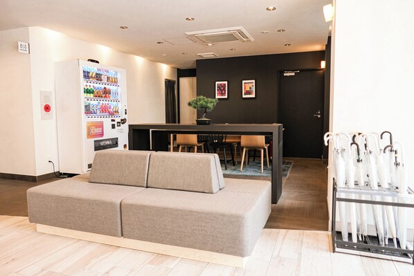 A modern hotel lobby with a sofa, vending machine, dining area, and umbrella rack.