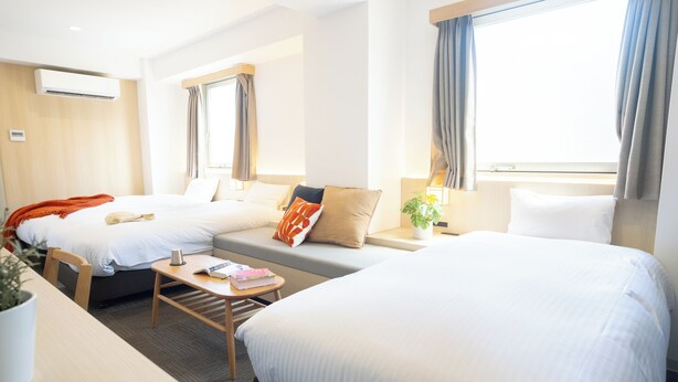 A hotel room with two beds, a sofa, a small table, and a potted plant. - WAYFARER Matsu (Osaka)