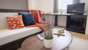 A modern hotel room with a sofa, a coffee table, a TV, and a small kitchenette. - WAYFARER Matsu (Osaka)