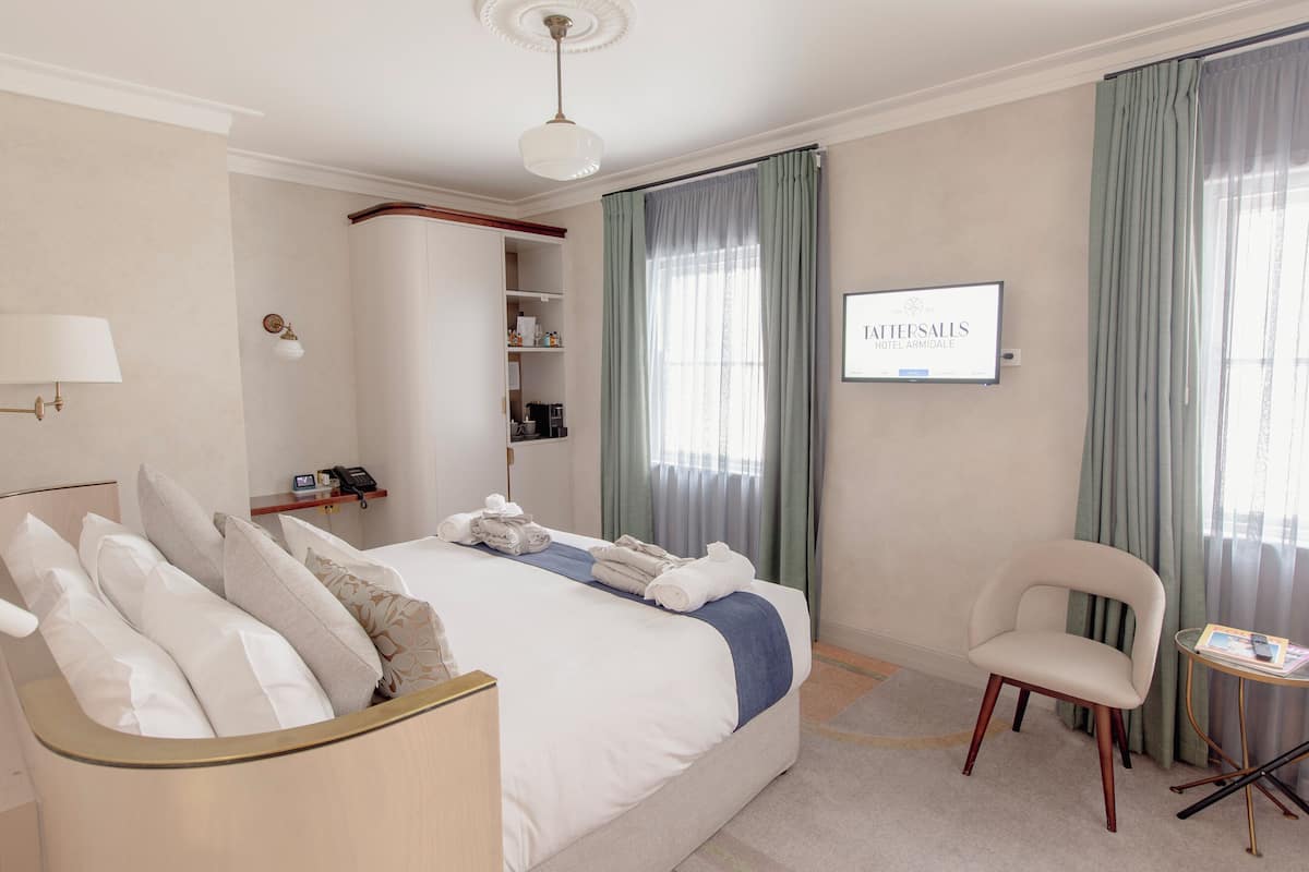 Habitación de hotel con una cama grande, una silla, un televisor y un minibar.