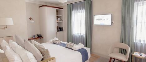 A hotel room with a large bed, a chair, a TV, and a minibar.