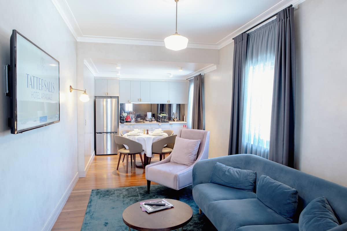 Una sala de estar moderna con un sofá azul, una mesa de centro redonda y una zona de comedor con una mesa y sillas blancas.