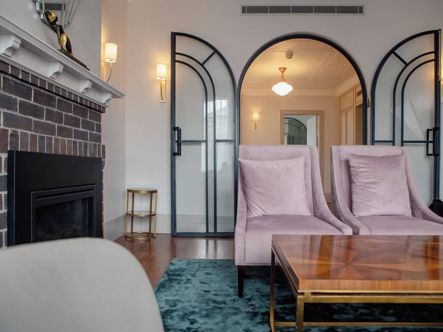 Uma sala de estar moderna com lareira de tijolos, dois poltronas rosa, uma mesa de centro de madeira e um tapete azul.