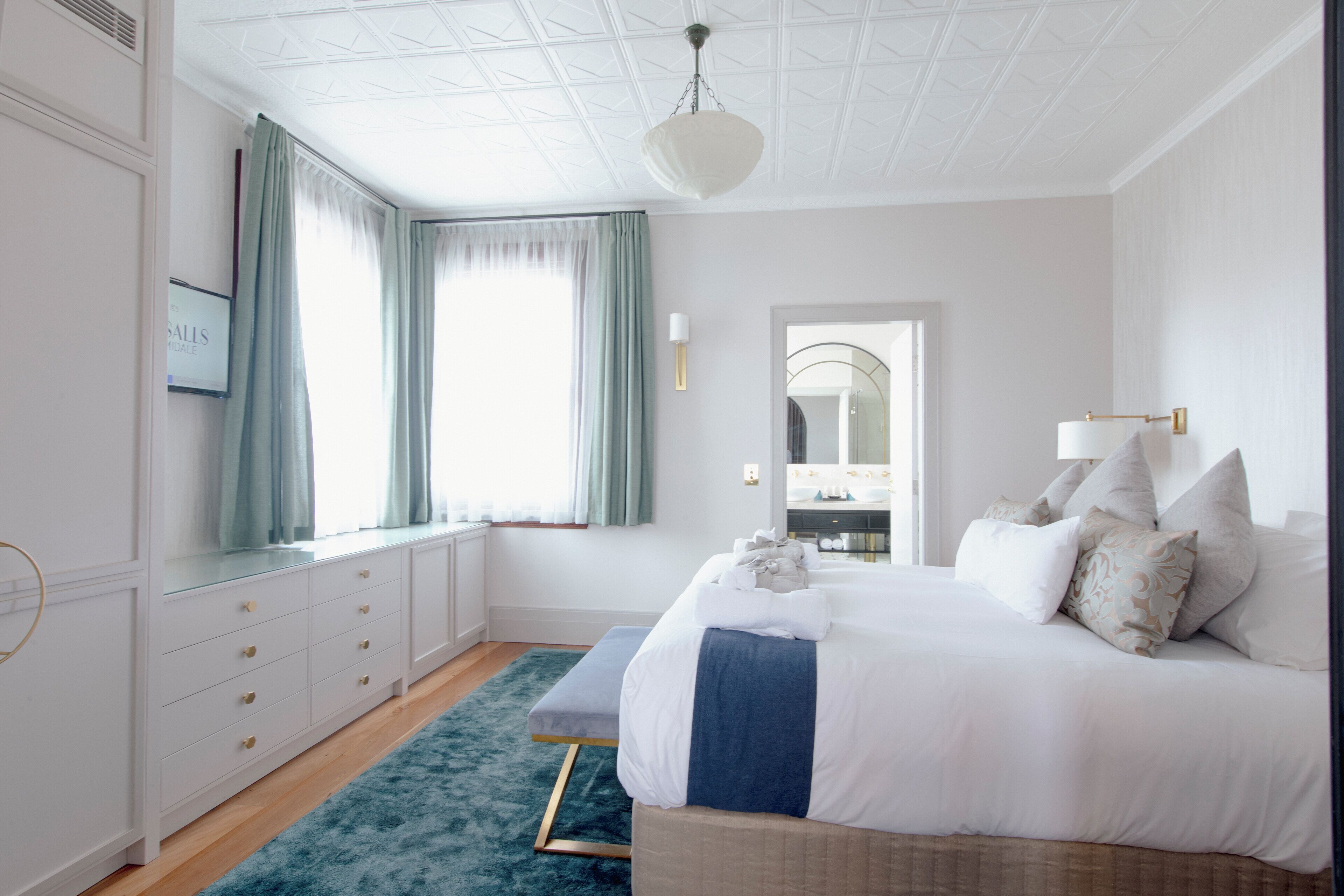 Een slaapkamer met een bed, een dressoir, een spiegel en een raam met gordijnen.
