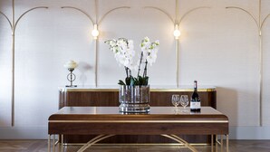 A wooden table with a vase of white orchids, a wine bottle, and a glass on it.