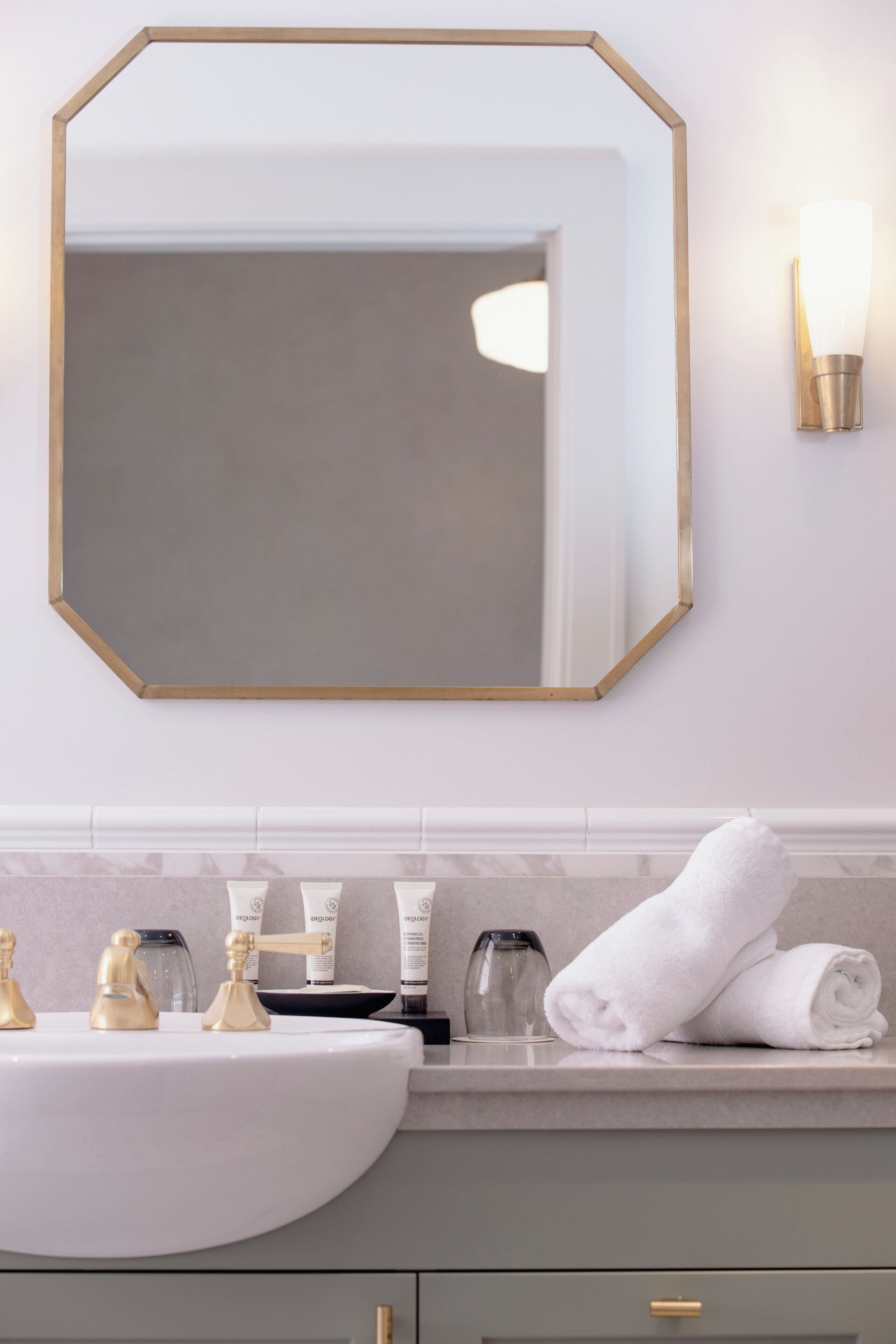A bathroom with a white sink, gold faucets, a large mirror with a gold frame, and a towel on the counter.