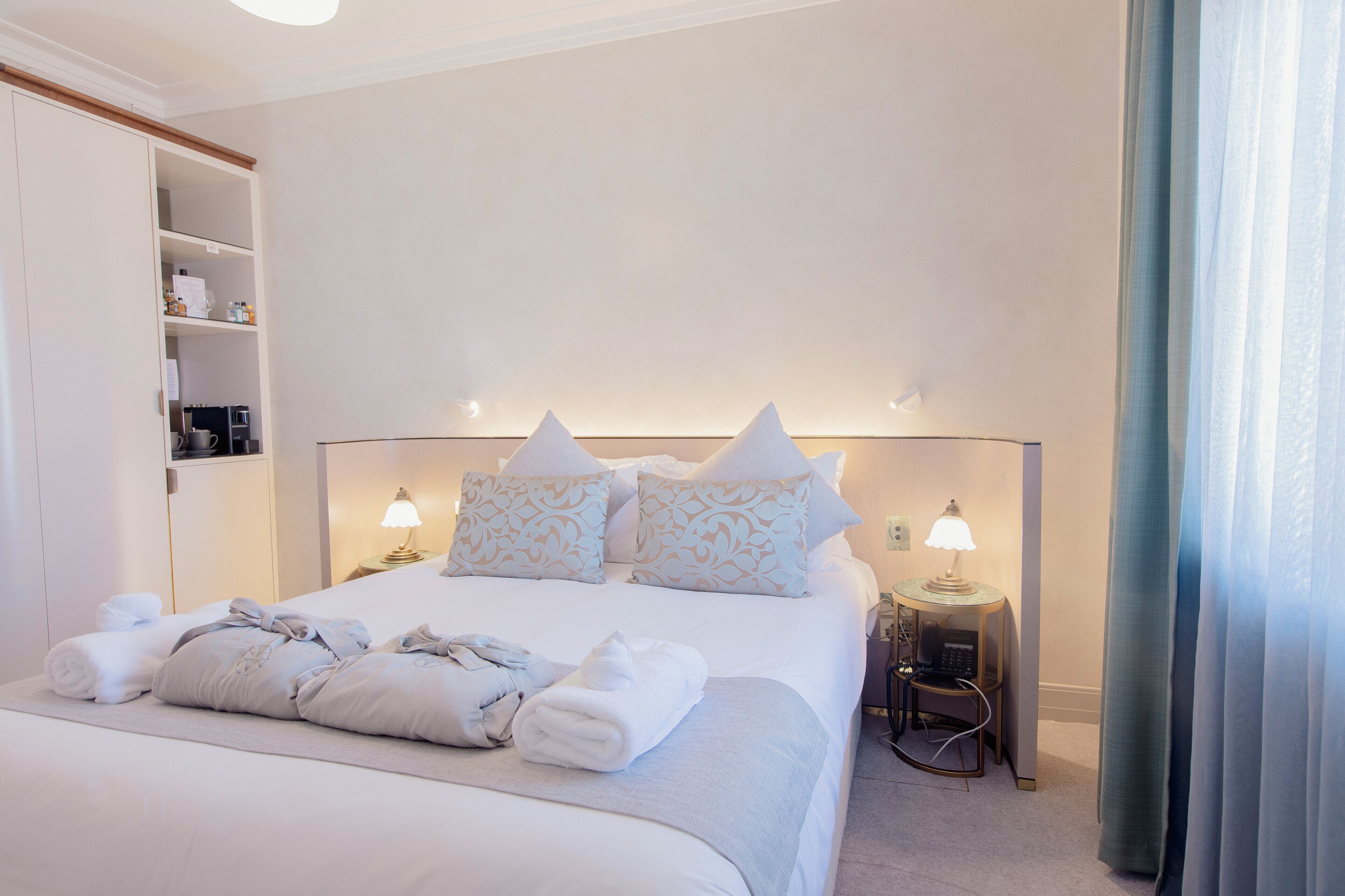 A neatly made bed with pillows and towels, a bedside table with a lamp, and a wardrobe.