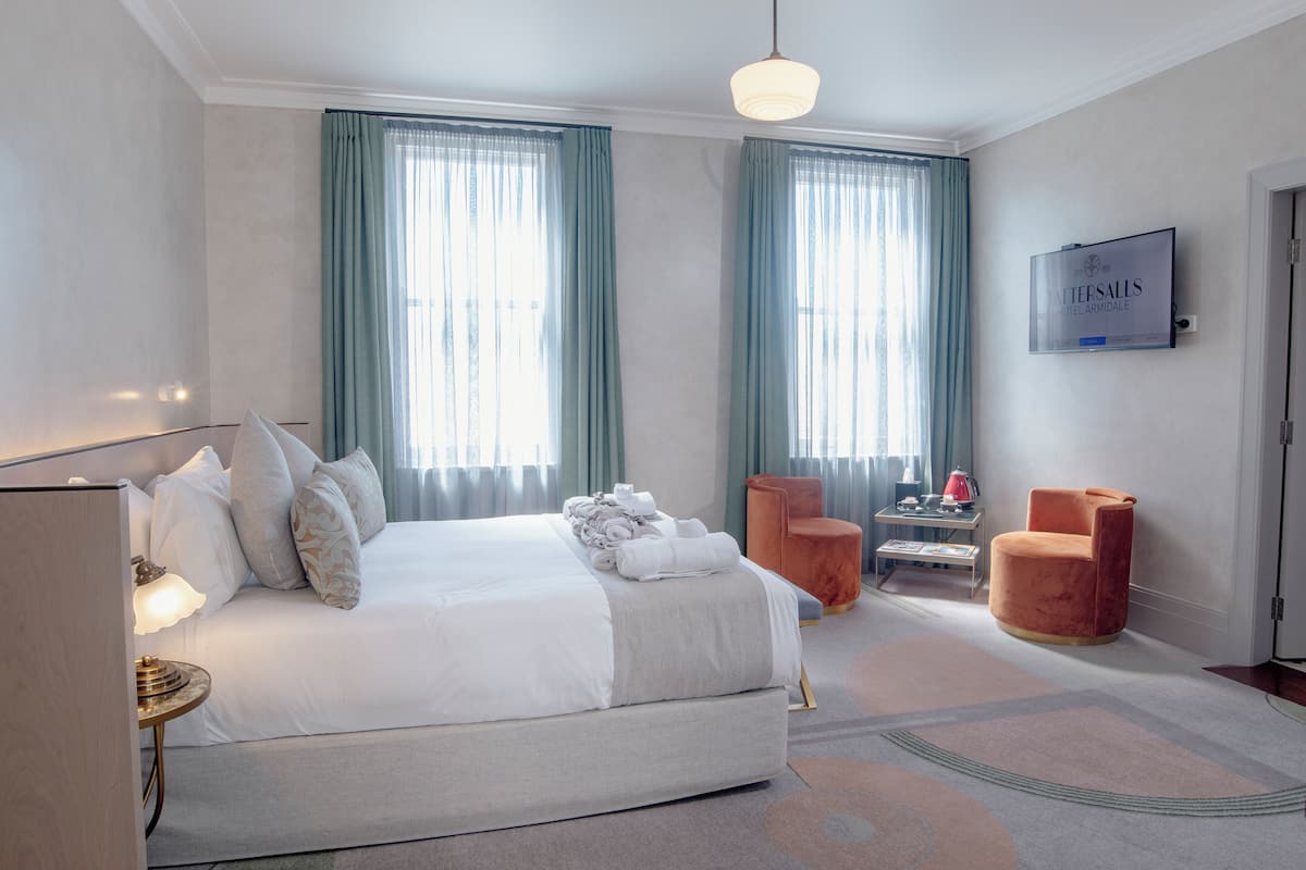 Habitación de hotel con una cama grande, dos sillas, un televisor y un escritorio con lámpara.