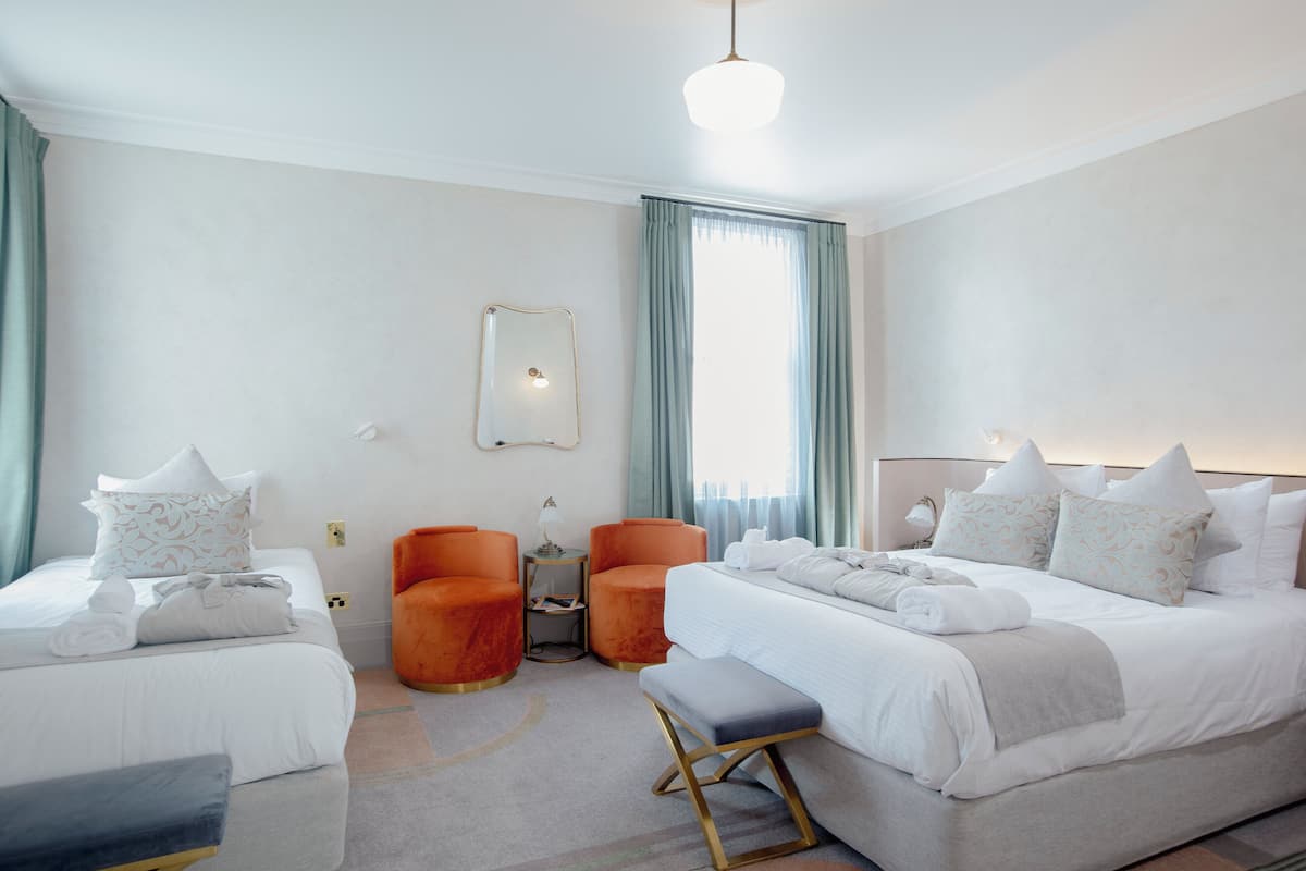 Una habitación de hotel con una cama grande, dos camas más pequeñas, un banco y dos sillones naranja.