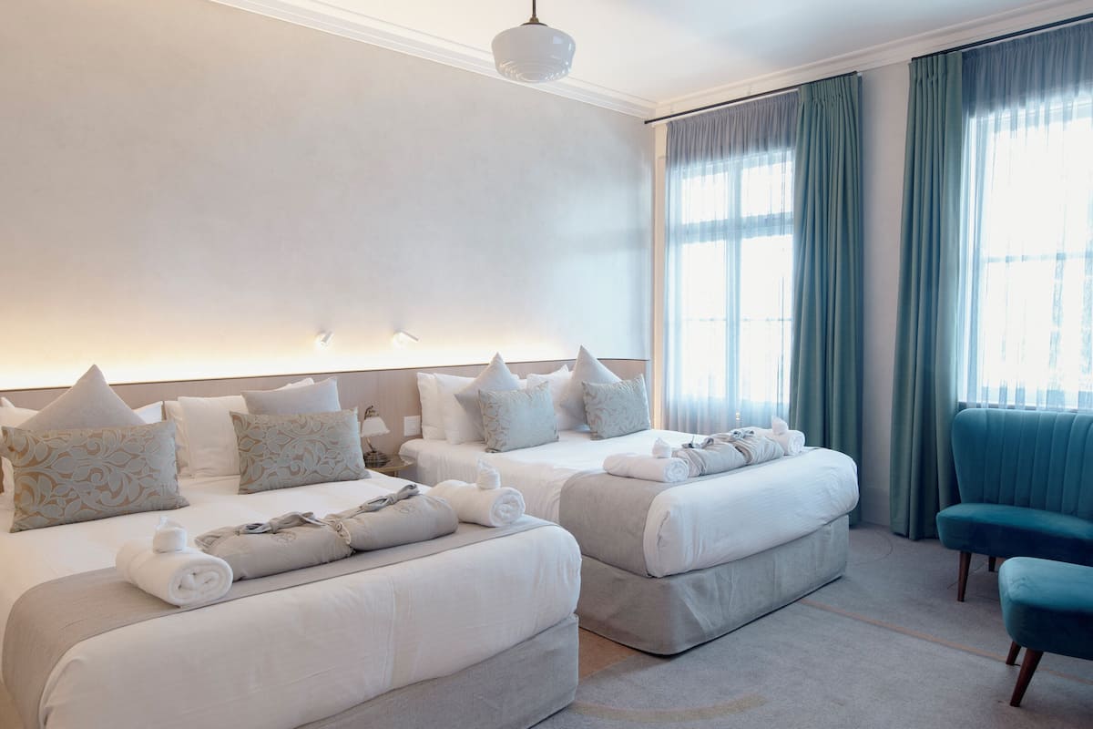 Una habitación de hotel con dos camas, un sofá y un amplio ventanal con cortinas.
