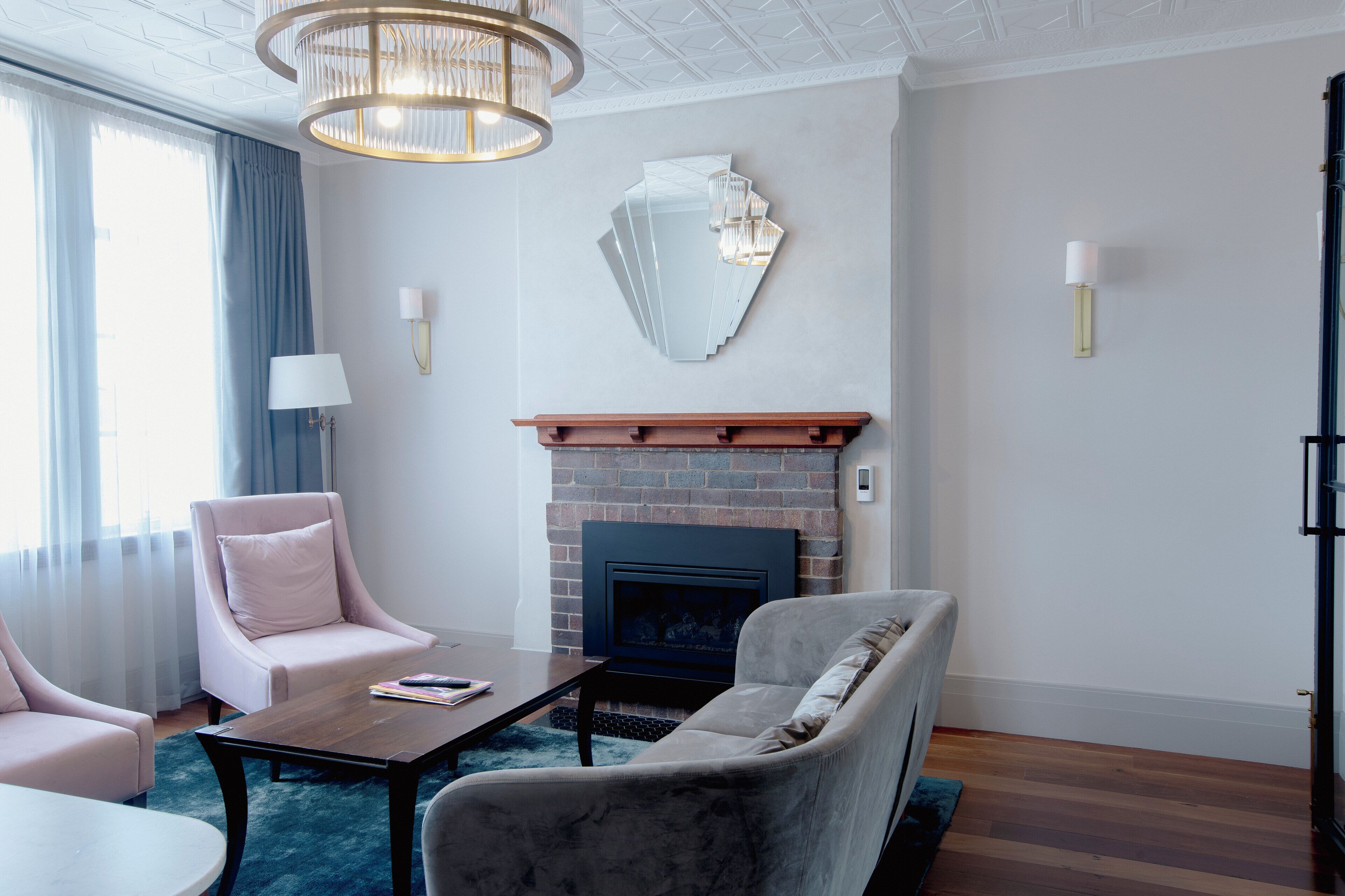A modern living room with a fireplace, two armchairs, a coffee table, and a chandelier.