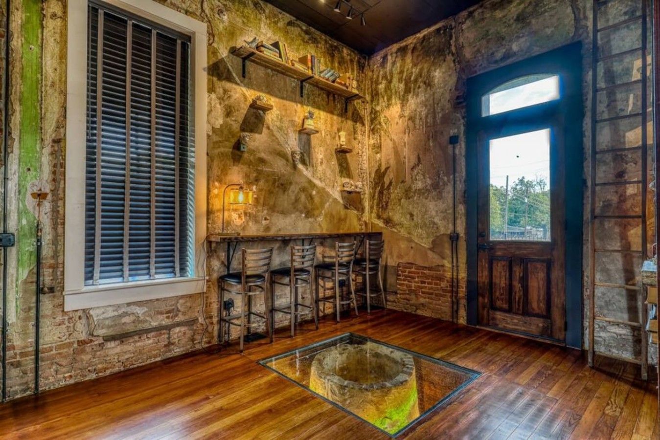 A rustic interior with exposed brick walls, a wooden bar area with stools, a large window, and a glass table centerpiece.