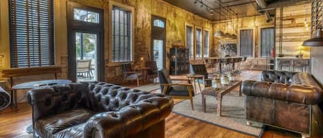 A spacious room with a large leather sofa, wooden flooring, and a rustic brick wall.