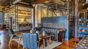 Un salon chaleureux avec un canapé en cuir, une table basse en bois et des fauteuils. Une bibliothèque remplie de livres est visible dans un coin.
