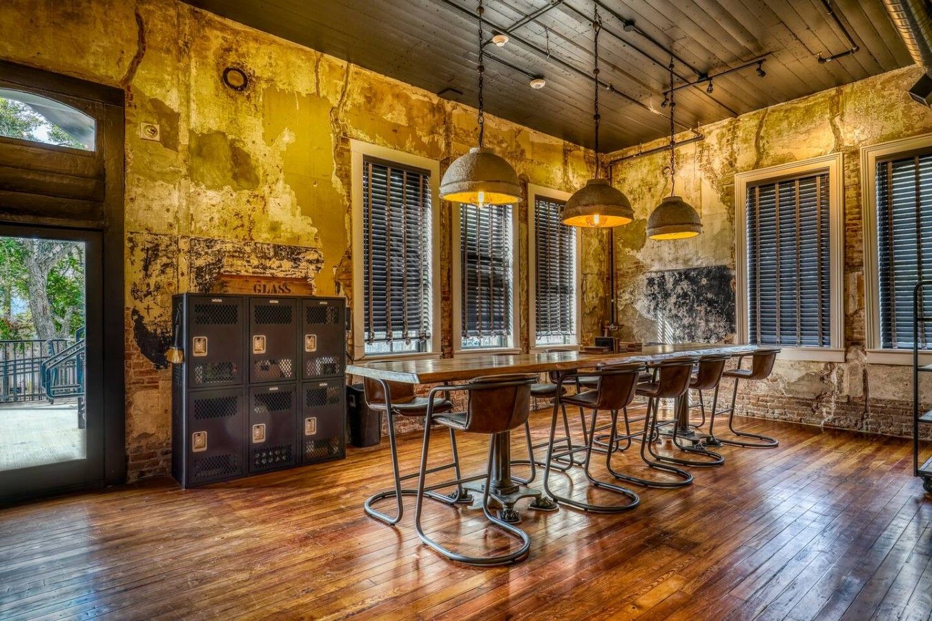 A rustic bar area with wooden flooring, metal bar stools, and pendant lighting.