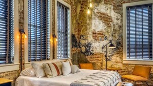 Une chambre à coucher avec un grand lit, plusieurs fenêtres équipées de stores, une lampe et une chaise.