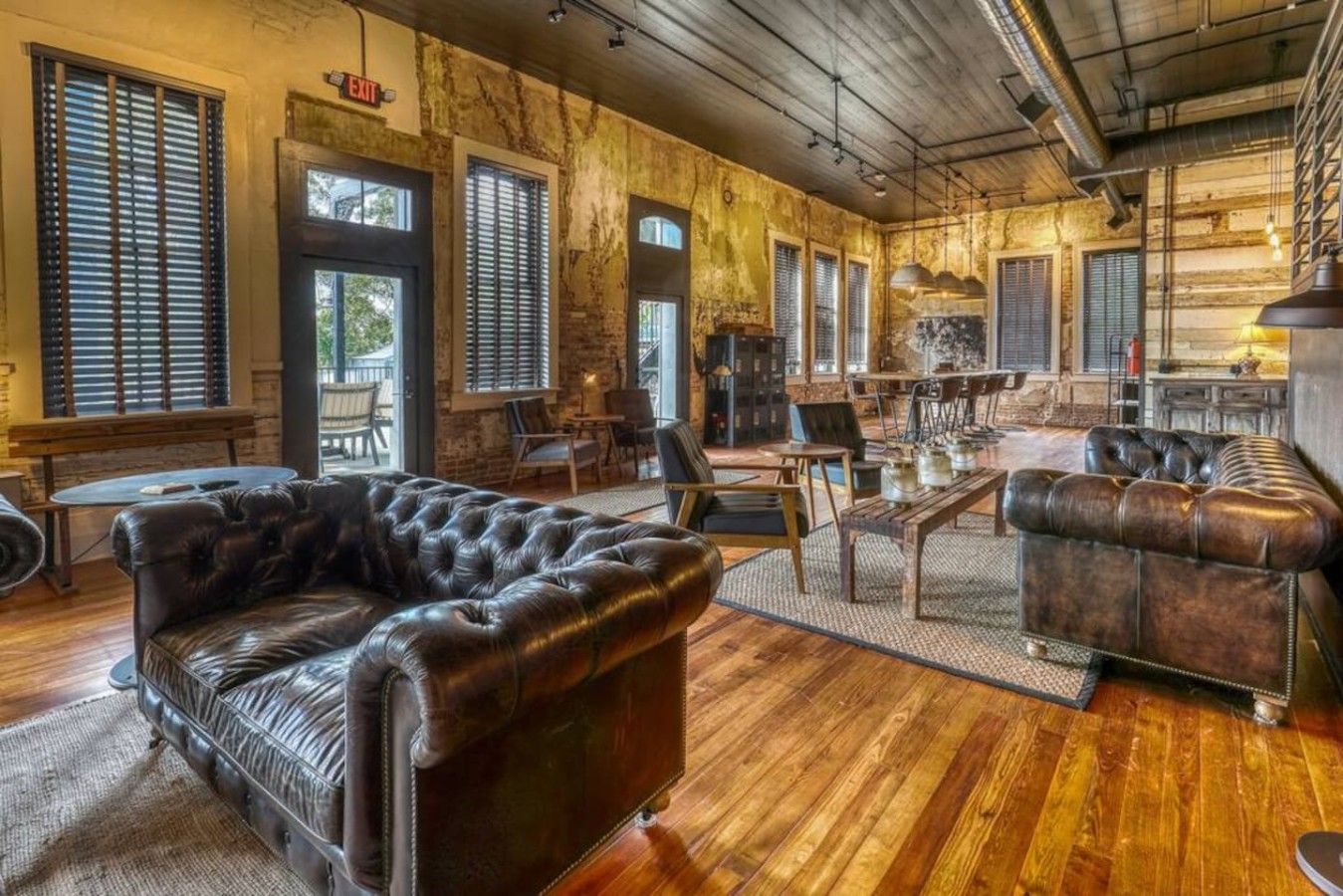 Une pièce spacieuse avec un canapé en cuir, un plancher en bois et de grandes fenêtres équipées de stores.