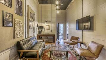 A spacious living room with a leather sofa, a coffee table, and a rug. There are framed pictures on the walls and a television mounted on the wall.