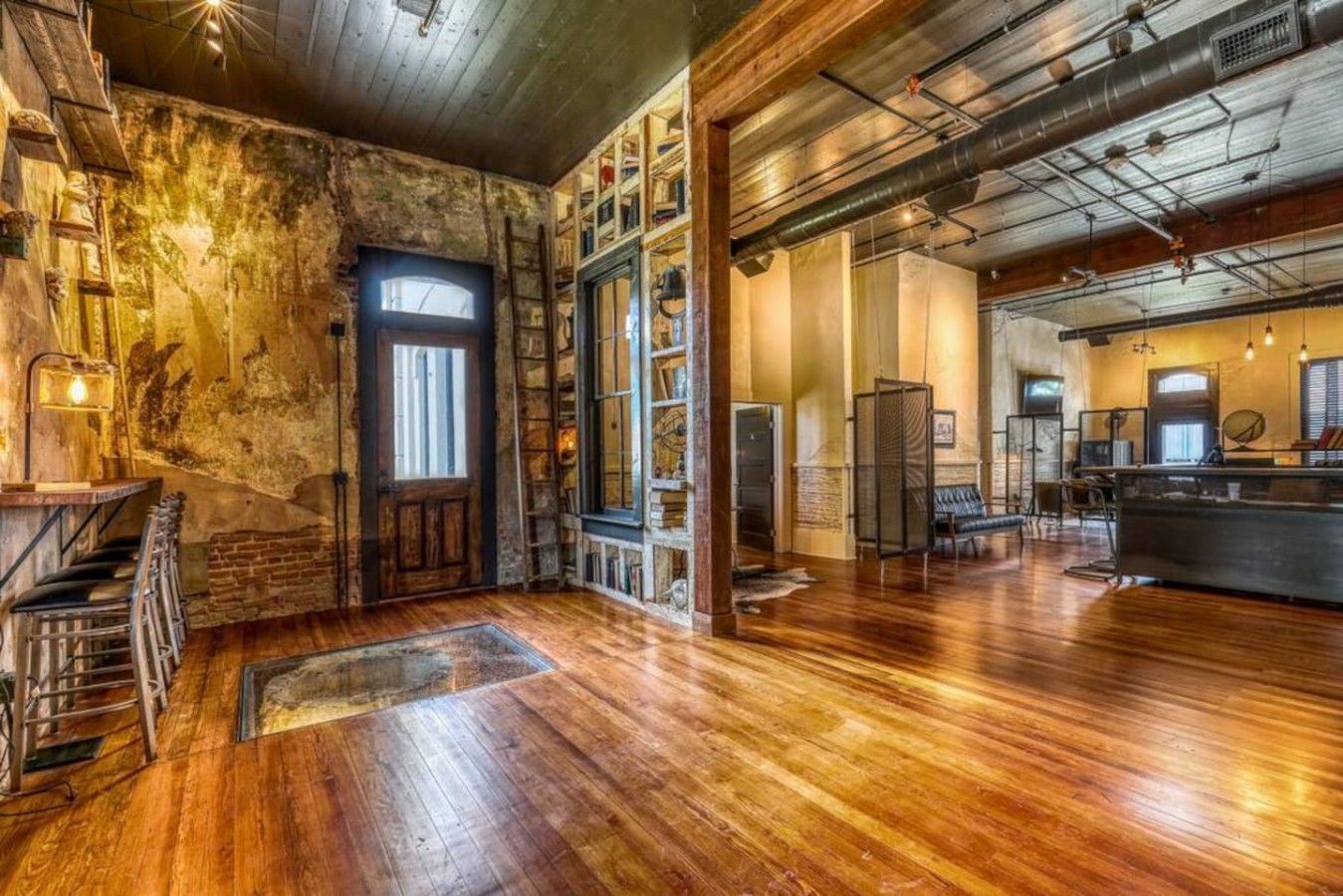 A spacious interior with a wooden staircase, a large open area with a wooden floor, and a bar area with seating.